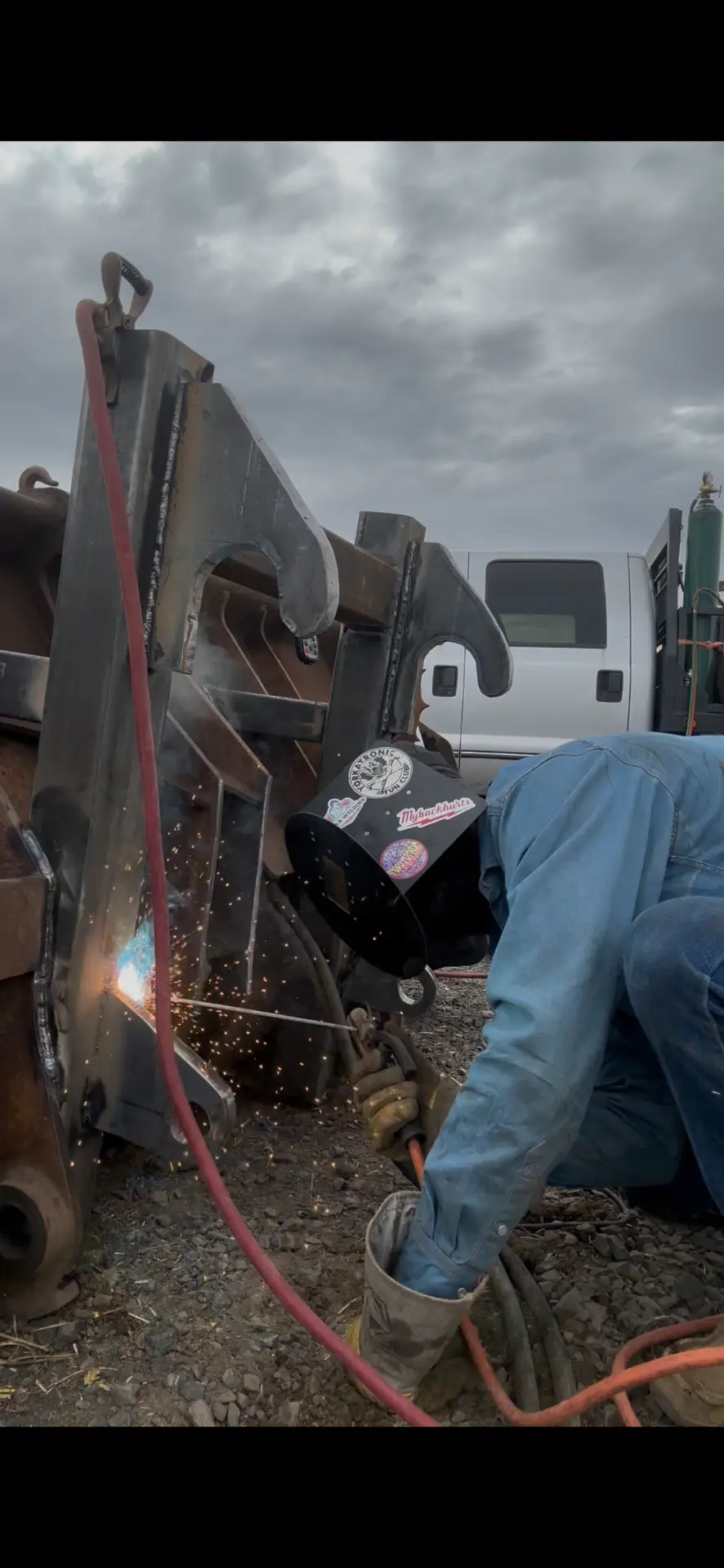 Welder in a protective hood welding heavy steel hook brackets onto a farm implement