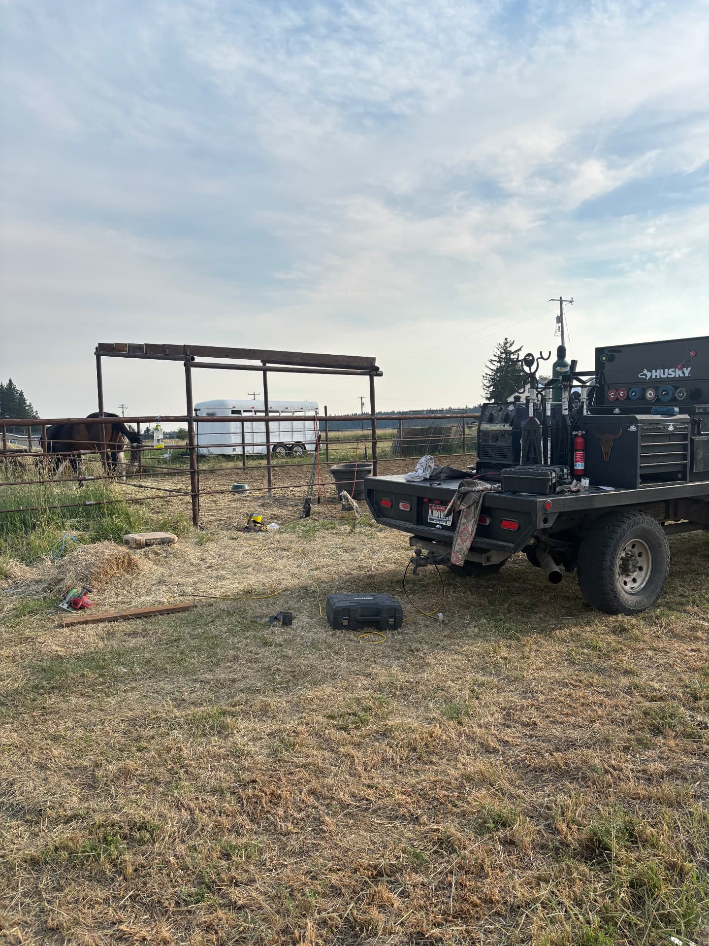 Kobar Welding mobile rig set up in a ranch pasture beside steel pipe corral panels and shelter framing under construction