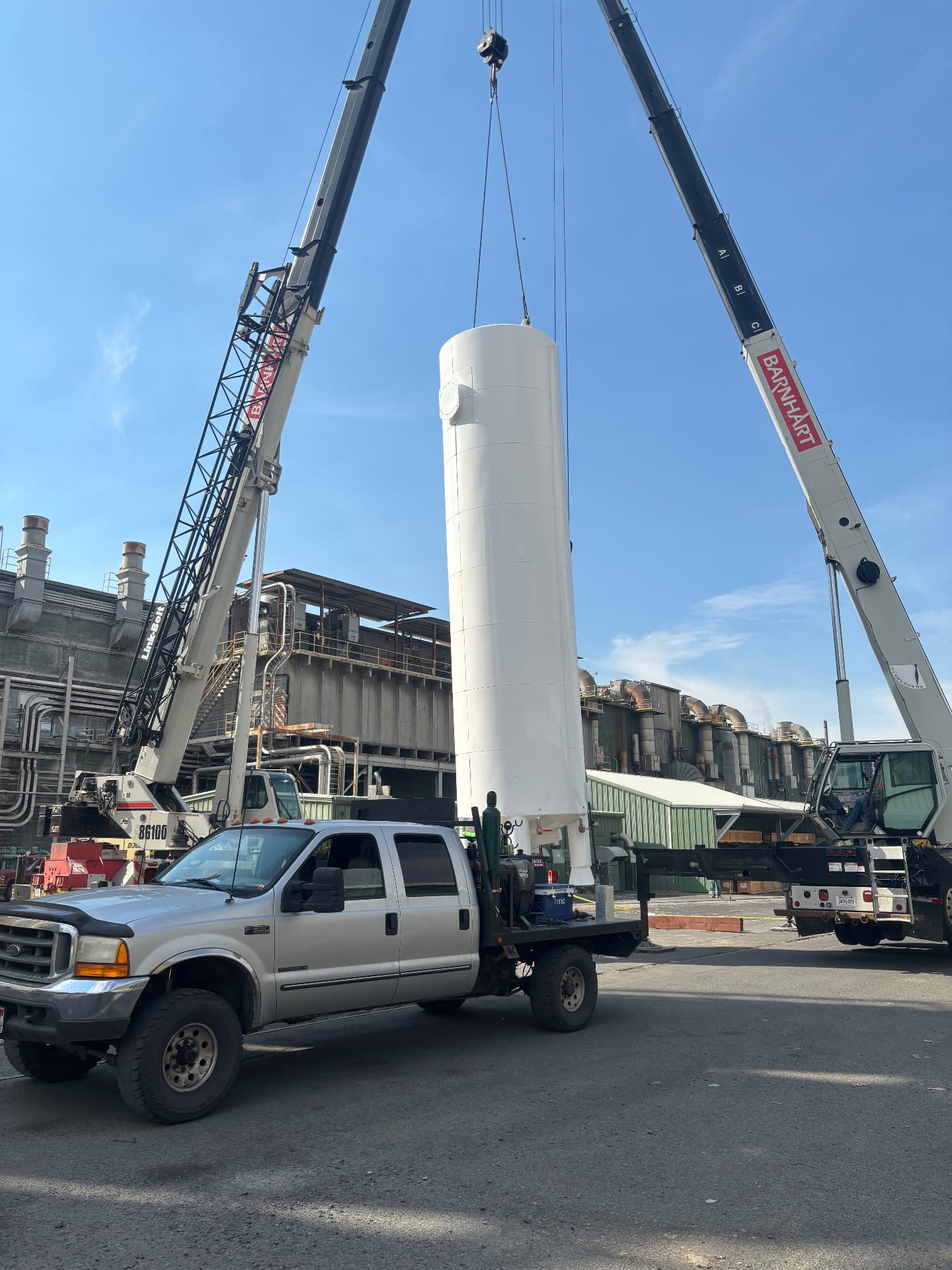 Large industrial tank lifted by cranes at an industrial facility